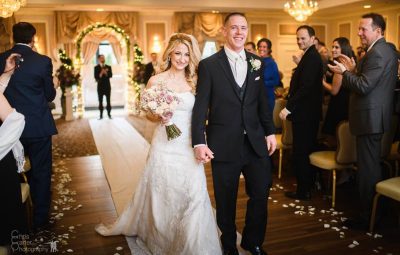 Beautiful bride woman in long white lace dress veil and elegant groom married couple hold hands walking along the boutique hall.