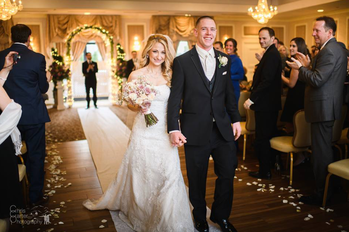 Beautiful bride woman in long white lace dress veil and elegant groom married couple hold hands walking along the boutique hall.