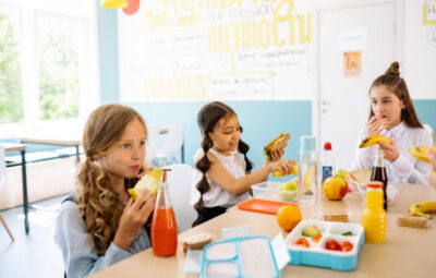 Three school kids sitting around the table and having their lunch, healthy meals can be seen.