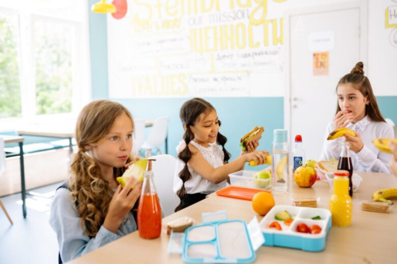 Three school kids sitting around the table and having their lunch, healthy meals can be seen.